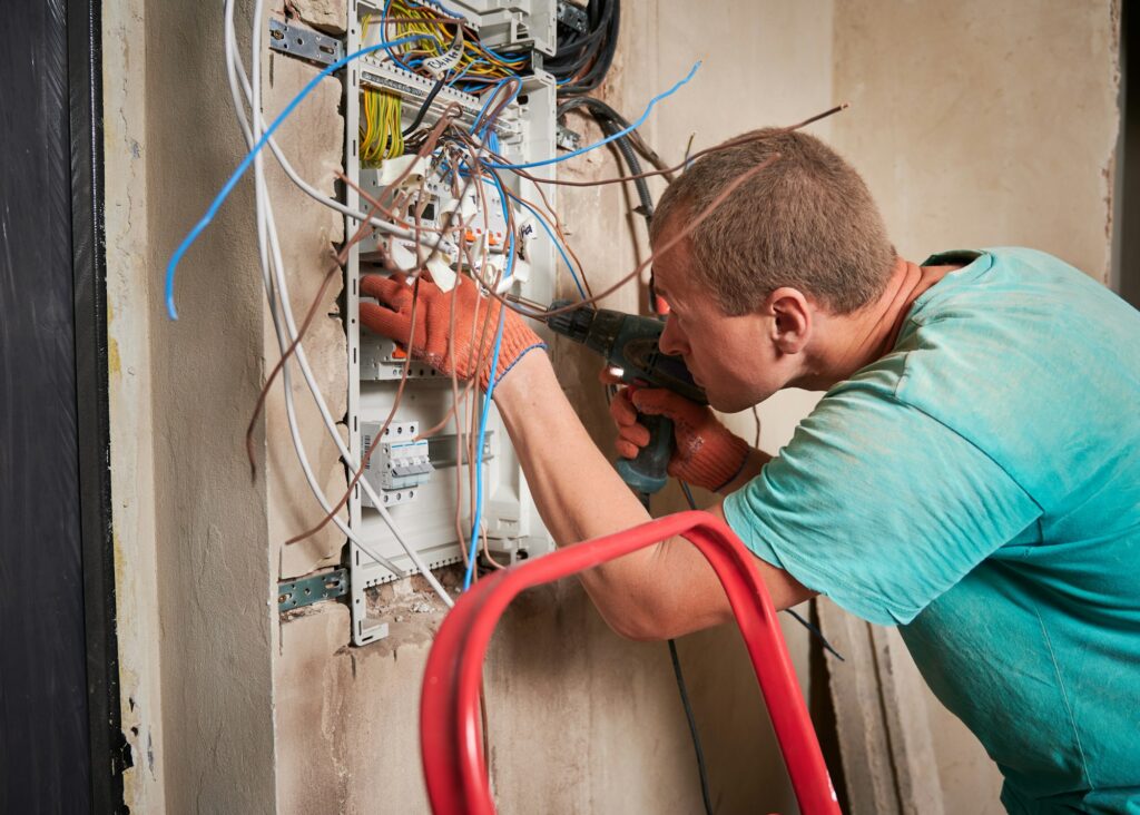 Male electrician repairing electrical panel with power drill.